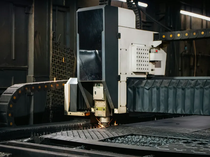 An industrial laser cutter working across a steel sheet.
