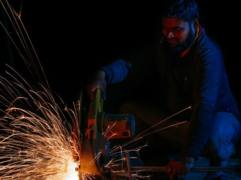 A welder working in the dark, sparks lighting the shop floor.