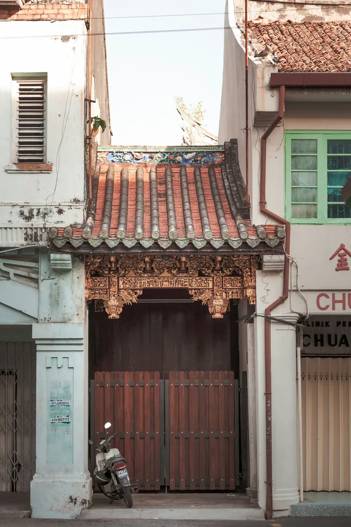 A weathered shophouse frontage with carved timber doors and a tiled roof.