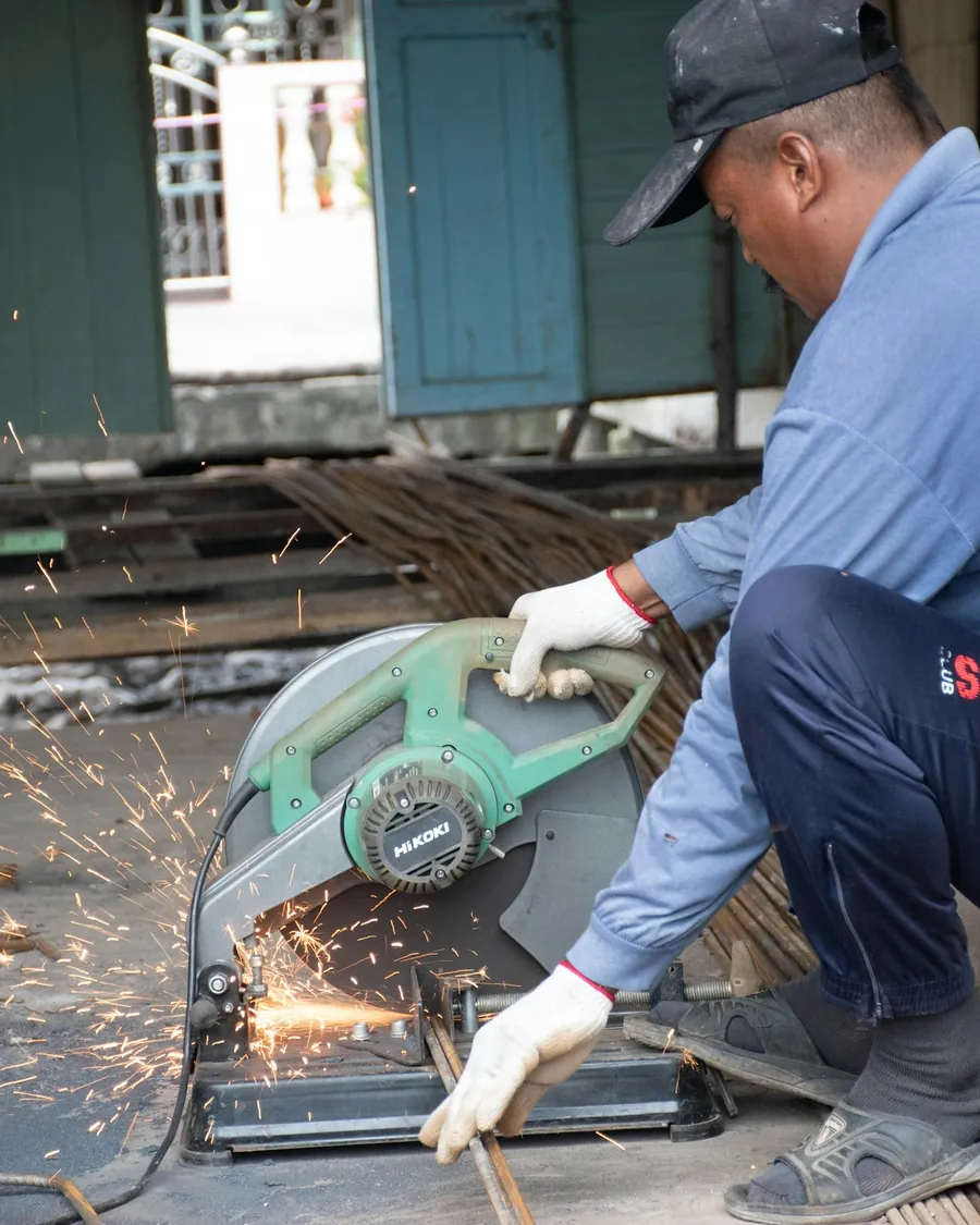 A worker in a blue shirt cutting steel with an angle grinder, sparks flying.