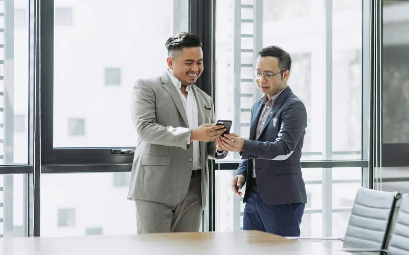 Two colleagues looking at a phone in a bright office.