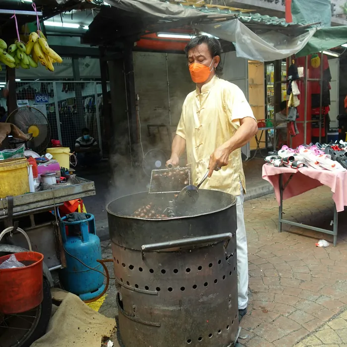 A street vendor roasting chestnuts in a large drum over an open flame.